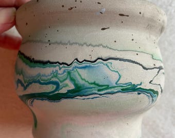 Può includere: Un piccolo vaso in ceramica arrotondato con una base opaca color bianco sporco e una consistenza maculata. L'esterno è decorato con un motivo vorticoso e marmorizzato di linee verdi, verde acqua e nere che avvolgono il centro.