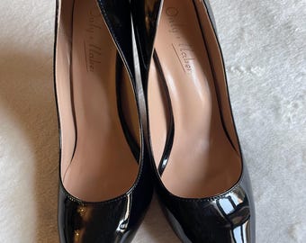 Può includere: Un paio di décolleté a punta in vernice nera con tacco a spillo alto. L'interno delle scarpe presenta una fodera beige chiaro con il nome del marchio Only Maker stampato in corsivo nero sulla zona del tallone del plantare.