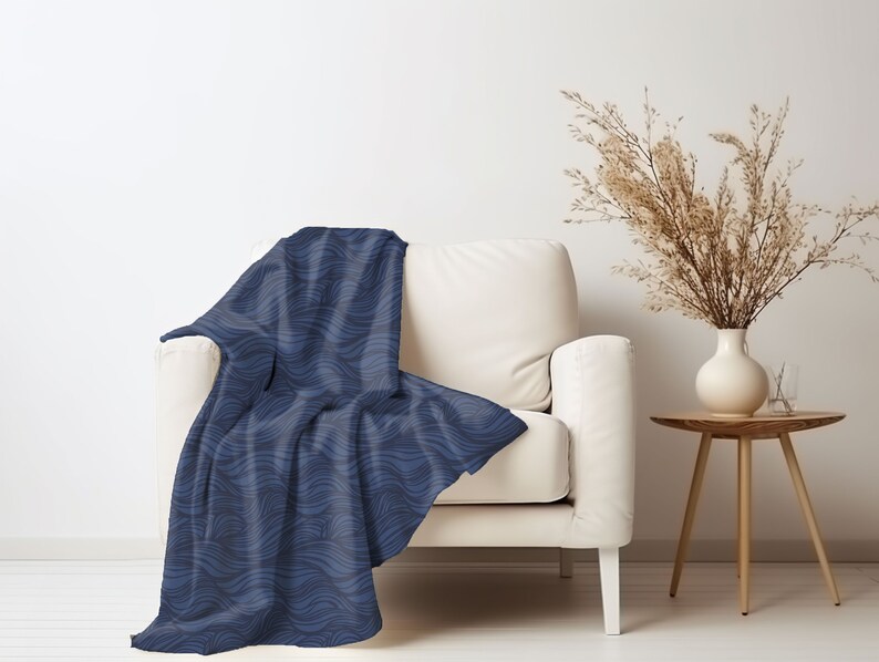 May include: A blue throw blanket with a wavy pattern draped over a white armchair. The blanket is made of soft, plush fabric and has a contemporary design.