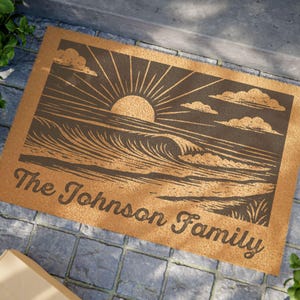 Könnte beinhalten: Eine rechteckige Fußmatte mit braunem Hintergrund und einer dunkelbraunen Grafik eines Sonnenuntergangs über Meereswellen. Der Text "The Johnson Family" ist in einer Schreibschrift gedruckt.