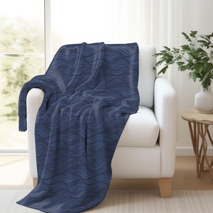 May include: A blue throw blanket with a wavy pattern, draped over a white armchair in a living room setting.