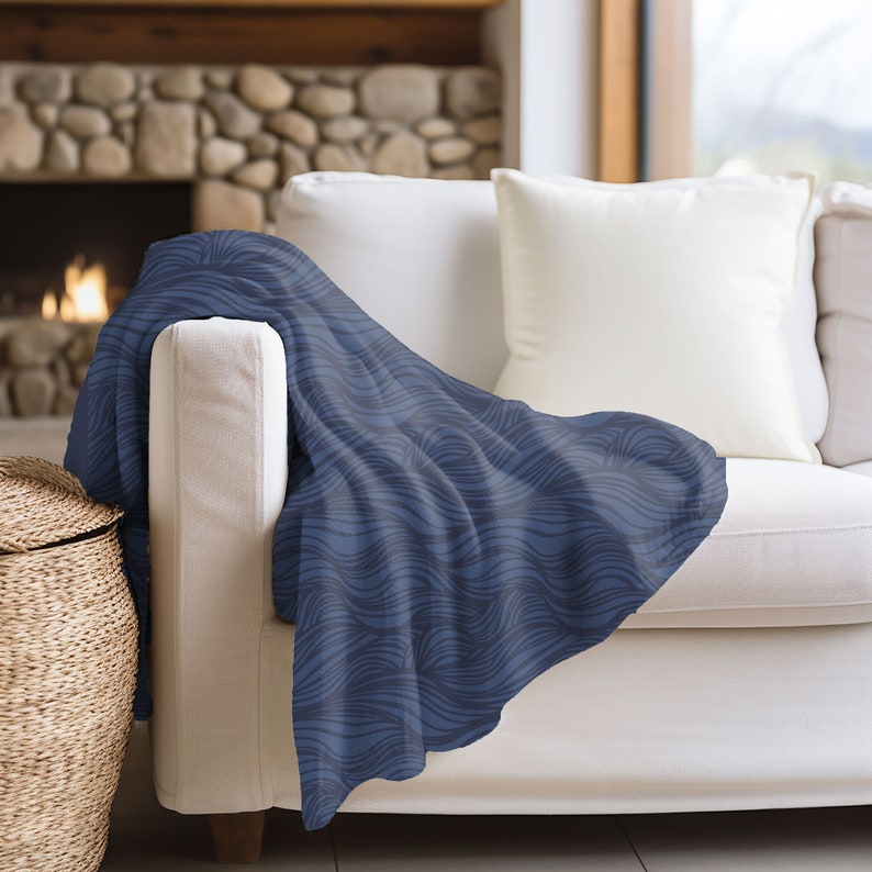 May include: A blue throw blanket with a wavy pattern draped over a white couch. The blanket is made of soft, plush fabric and has a subtle sheen.