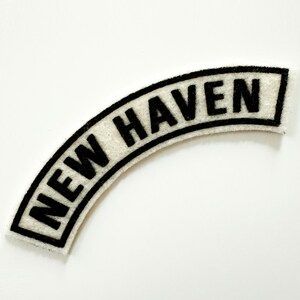 May include: White fabric patch with black embroidered text that reads "NEW HAVEN".