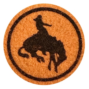 May include: A brown leather circle with a black outline and a silhouette of a cowboy riding a bucking bronco.