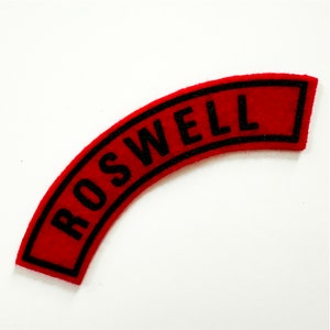 May include: Red felt patch with black outline and the word "ROSWELL" in black lettering.