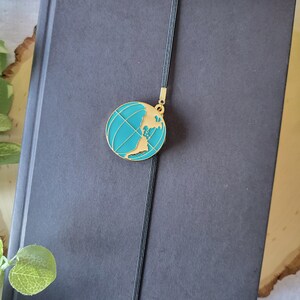 Peut inclure: Un carnet noir avec un marque-page globe bleu turquoise. Le marque-page est attaché au carnet avec une ficelle noire.