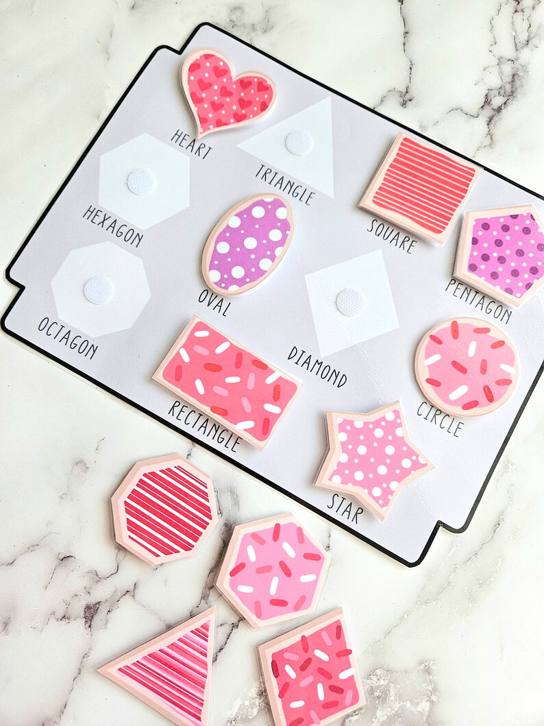 Pode incluir: Um conjunto de 10 formas de feltro coloridas com padr&otilde;es rosa e branco. As formas incluem um cora&ccedil;&atilde;o, um tri&acirc;ngulo, um quadrado, um oval, um pent&aacute;gono, um hex&aacute;gono, um oct&oacute;gono, um diamante, um c&iacute;rculo e uma estrela. Cada forma tem uma forma de feltro branca correspondente com um ponto de velcro para combinar.
