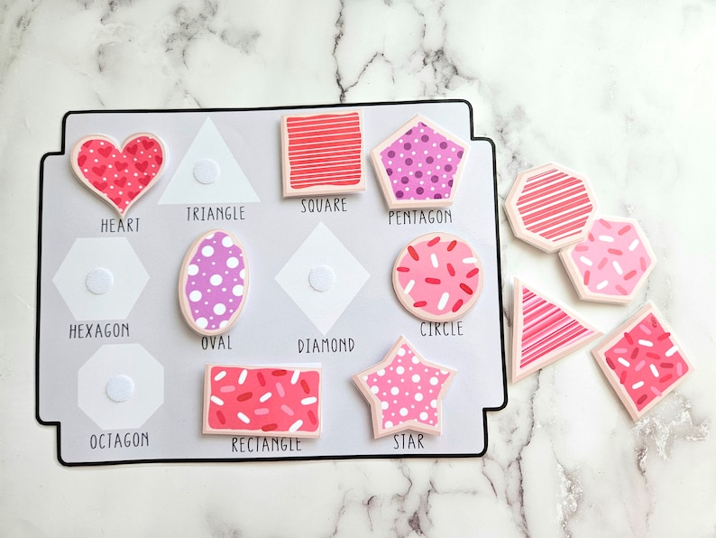 Pode incluir: Um brinquedo educativo rosa e branco com diferentes formas, incluindo um cora&ccedil;&atilde;o, um tri&acirc;ngulo, um quadrado, um pent&aacute;gono, um hex&aacute;gono, um oval, um diamante, um c&iacute;rculo, um oct&oacute;gono, um ret&acirc;ngulo e uma estrela. Cada forma tem um padr&atilde;o diferente.