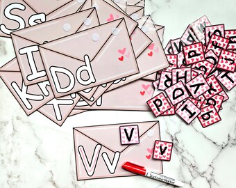 Op de afbeelding: Roze enveloppen met witte letters en harten, en roze lettertegels met harten, voor een Valentijnsdag-alfabetactiviteit.