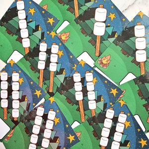 May include: A set of printable cards featuring a campfire scene with a stick figure roasting marshmallows. The cards have a blue and green background with yellow stars and a campfire in the bottom right corner. The cards are blank on the bottom for writing.
