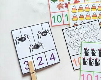 May include: A set of Halloween-themed counting cards featuring images of spiders, ghosts, pumpkins, candy corn, and cats. The cards have numbers printed on them, and there are clothespins to help with counting.