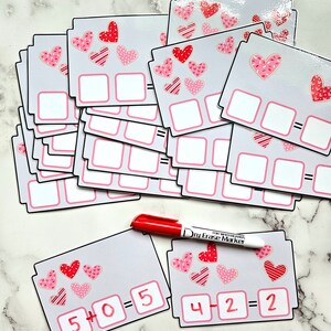 May include: A set of Valentine's Day themed math flashcards with hearts and the equations 5 + 0 = 5 and 4 - 2 = 2 written on them. A red dry erase marker is also included.