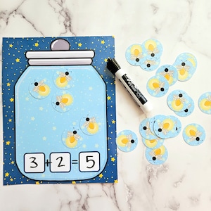 Op de afbeelding: Een blauw en wit printbaar activiteitenblad met een afbeelding van een pot vol met vuurvliegjes. Het blad bevat de vergelijking 3 + 2 = 5. Er zijn ook verschillende vuurvliegjes stickers op een wit oppervlak.