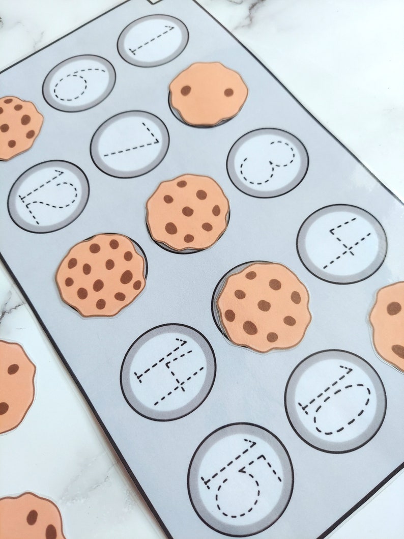 May include: A gray and white learning activity with a cookie theme. The activity has 12 circles with dotted lines for tracing numbers. There are 10 brown cookies with chocolate chips on top.