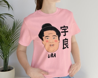 May include: Pink t-shirt with a cartoon illustration of a sumo wrestler with the Japanese characters "Ura" and "Judo" printed on the front.