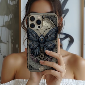 May include: A smartphone case featuring a detailed illustration of a dark blue moth with intricate wing patterns. The case has a vintage, ornate design with floral and clock elements, and a gold border. The overall aesthetic is gothic and artistic.