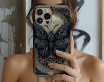 May include: A smartphone case featuring a detailed illustration of a dark blue moth with intricate wing patterns. The case has a vintage, ornate design with floral and clock elements, and a gold border. The overall aesthetic is gothic and artistic.