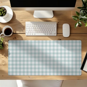 May include: A light blue and white checkered pattern desk mat. The mat is rectangular and covers a portion of a wooden desk. A computer keyboard, mouse, and monitor are visible, along with a cup of coffee and a small potted plant.