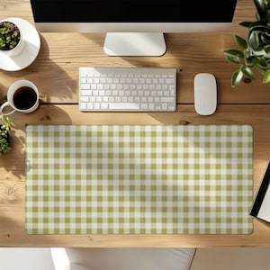 May include: A rectangular desk mat with a green and white gingham pattern. The mat is on a wooden desk, with a keyboard, mouse, and monitor visible. A cup of coffee and a small potted plant are also on the desk.
