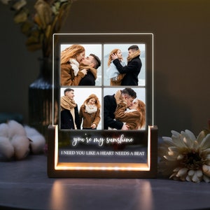 May include: A wooden photo frame with a clear acrylic insert displaying four photos of a couple. The frame has a white inscription that reads "you're my sunshine I need you like a heart needs a beat".