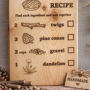 Pu&ograve; includere: Targa in legno con la scritta "DIRT PIE RECIPE" incisa in alto. La ricetta comprende rametti, pigne, ghiaia e dente di leone. &Egrave; attaccata una piccola etichetta con la scritta "HANDMADE".
