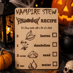 Pu&ograve; includere: Cartello di ricetta di Halloween in legno per "Vampire Stew". Il cartello include gli ingredienti della ricetta: foglie, dente di leone, sabbia e acqua. Il cartello &egrave; circondato da decorazioni di Halloween, tra cui zucche e un teschio.