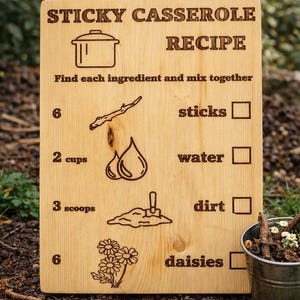 Pu&ograve; includere: Un cartello di legno con la scritta "RICETTA CASSERUOLA APPICCICOSA" e istruzioni per un gioco per bambini. Il cartello include illustrazioni di ingredienti come bastoncini, acqua, terra e margherite. Un piccolo secchio di metallo con bastoncini e fiori &egrave; sullo sfondo.