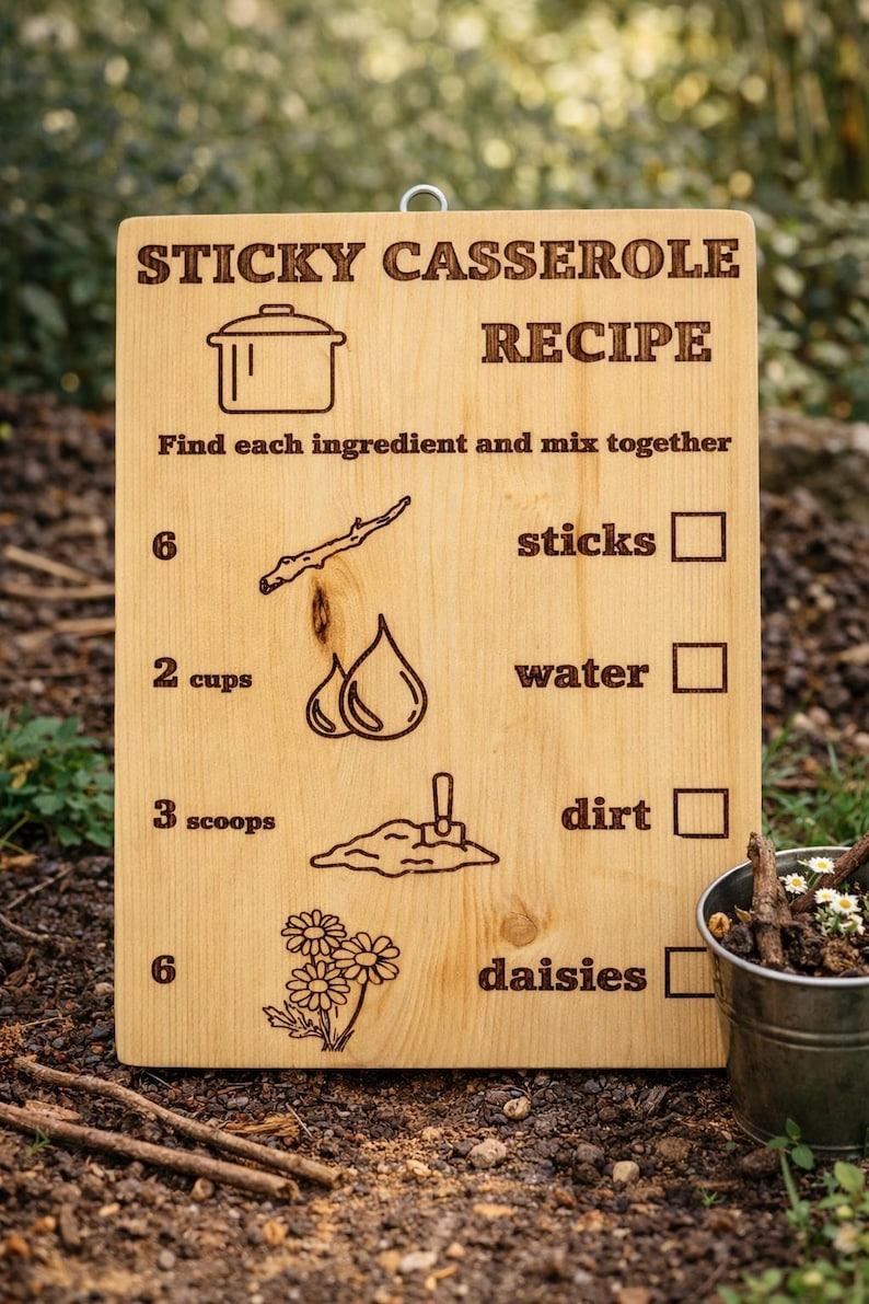 Pu&ograve; includere: Un cartello di legno con la scritta "RICETTA CASSERUOLA APPICCICOSA" e istruzioni per un gioco per bambini. Il cartello include illustrazioni di ingredienti come bastoncini, acqua, terra e margherite. Un piccolo secchio di metallo con bastoncini e fiori &egrave; sullo sfondo.