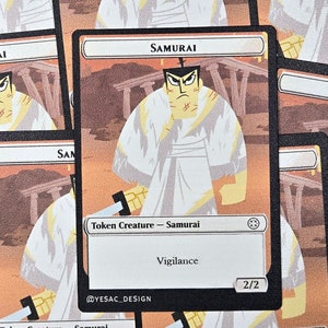May include: A white and orange card with a black border. The card features a cartoon samurai with a white robe and a red headband. The card text reads "Samurai" and "Token Creature - Samurai". The card also has the text "Vigilance" and "2/2".