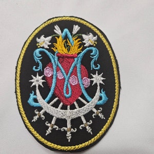 May include: An embroidered patch with a black background and a gold border. The centre of the patch features a stylised image of the Virgin Mary's heart, surrounded by swords, a crescent moon, and lilies.