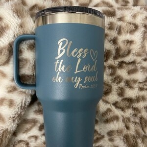 Puede incluir: Una taza de viaje de acero inoxidable azul con asa. Tiene una inscripci&oacute;n blanca que dice "Bless the Lord oh my soul Psalm 103:1".