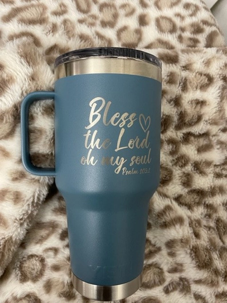 Puede incluir: Una taza de viaje de acero inoxidable azul con asa. Tiene una inscripci&oacute;n blanca que dice "Bless the Lord oh my soul Psalm 103:1".