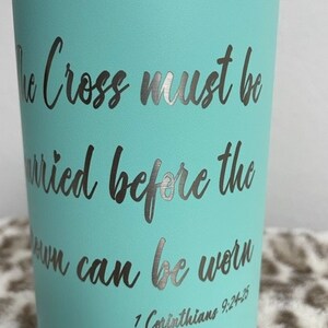 Puede incluir: Un vaso azul turquesa con una inscripci&oacute;n plateada que dice "The Cross must be carried before the crown can be worn 1 Corinthians 9:24-25".