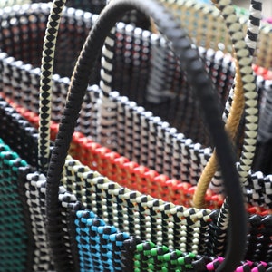 May include: Close-up of a stack of colorful woven baskets with black and white striped handles. The baskets are made of a thick, woven material and have a variety of colors, including orange, red, blue, green, and pink.