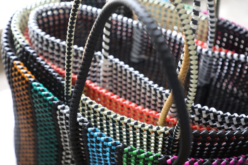 May include: Close-up of a stack of colorful woven baskets with black and white striped handles. The baskets are made of a thick, woven material and have a variety of colors, including orange, red, blue, green, and pink.