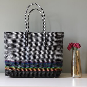 May include: Black and white tote bag with a rainbow stripe design. The bag has two black and white striped handles.