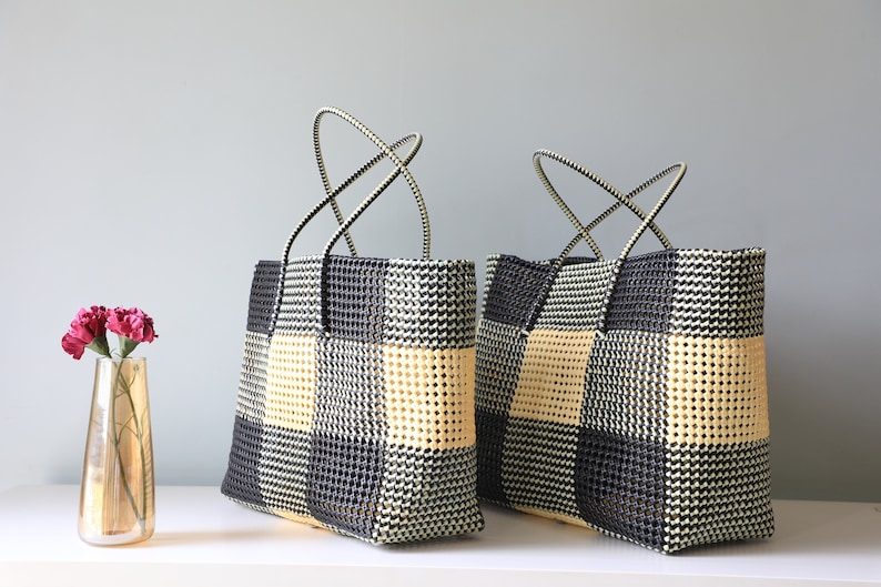 May include: Two black and cream checkered tote bags with black handles. The bags are made of woven plastic and have a square shape.