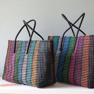 May include: Two colorful striped tote bags with black handles. The bags are made of woven plastic and have a black background with stripes of pink, orange, green, blue, and silver.