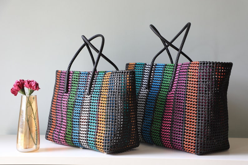 May include: Two colorful striped tote bags with black handles. The bags are made of woven plastic and have a black background with stripes of pink, orange, green, blue, and silver.
