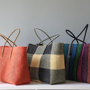 May include: Four colorful woven tote bags with different patterns. The bags have black, white, orange, green, blue, and pink stripes and checkered patterns. The bags have brown and black handles.
