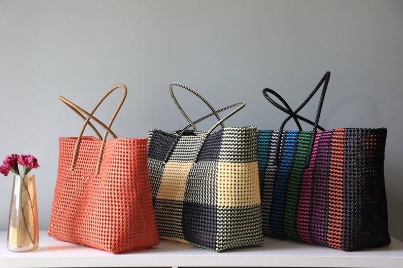 May include: Four colorful woven tote bags with different patterns. The bags have black, white, orange, green, blue, and pink stripes and checkered patterns. The bags have brown and black handles.