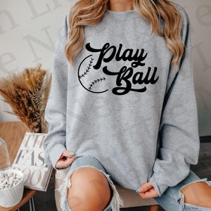 May include: A gray sweatshirt with the text "Play Ball" in black lettering and a baseball graphic.