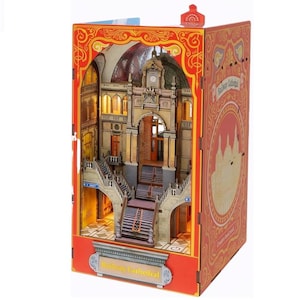 Puede incluir: Un rincón de libro detallado e iluminado de la Catedral Ferroviaria. La escena en miniatura presenta una gran escalera, una torre del reloj y puertas arqueadas. El exterior es rojo con patrones decorativos y el texto "Railway Cathedral".