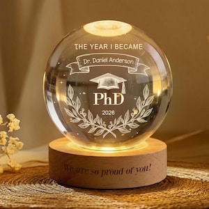 May include: A white ceramic mug with a black handle and the text "But First, Coffee" in a black, handwritten-style font. The mug is on a white surface.