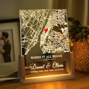 May include: A personalized illuminated map of New York City, with a red heart marking a location in Central Park. The map is etched on a clear acrylic panel, set in a wooden base. Text reads "WHERE IT ALL BEGAN" and names "Daniel & Olivia" with a date.