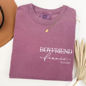 May include: A mauve colored t-shirt with the text "Boyfriend fiance" and the date "01.23.2025" printed in white.