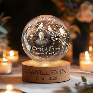 May include: A clear glass globe with a photo of a man, two birds, and the text "Always & Forever in our hearts." The globe sits on a wooden base engraved with "DANIEL JOHN" and the years "1946 - 2026."