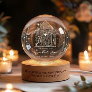 May include: A clear glass globe with a map of a house etched inside, resting on a wooden base. The globe is illuminated from below, displaying the text "Our First Home" and the address "123 Madison Ave, New York, NY".