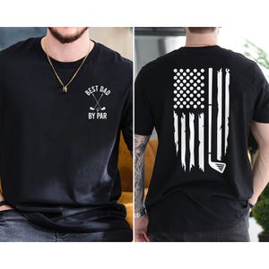 Peut inclure: T-shirt noir avec un motif blanc sur le devant qui dit "Best Dad By Par" et un motif blanc au dos qui repr&eacute;sente un club de golf et des balles de golf en forme de drapeau am&eacute;ricain.