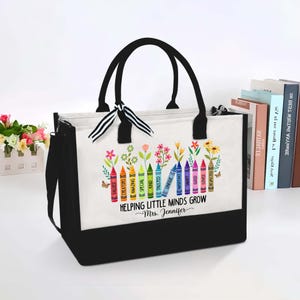Puede incluir: Bolsa de tela negra y blanca con un dise&ntilde;o de crayones de colores y el texto "Helping Little Minds Grow - Mrs. Jennifer".